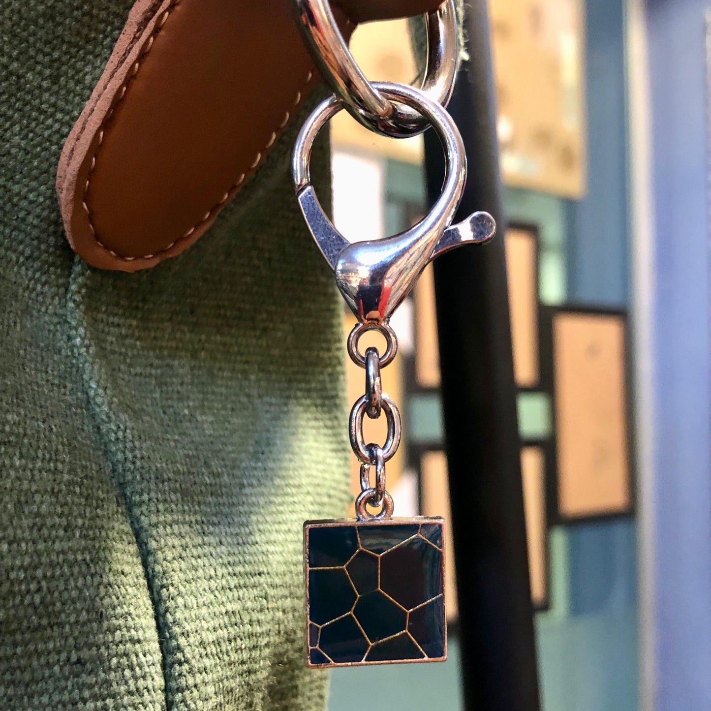 Silver keychain with a geometric design attached to a textured surface.