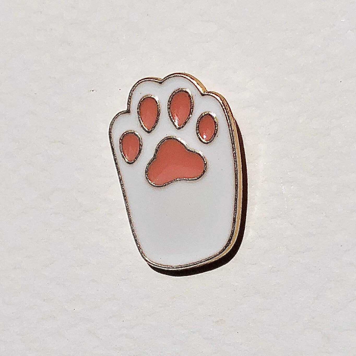 Paw print-shaped pin with red pads on a light gray background