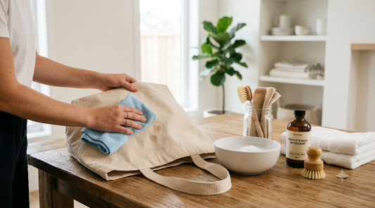 Person gently spot cleaning a beige canvas tote bag using mild soap and a soft cloth on a wooden table.