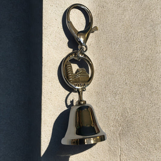 Metallic bell keychain with a logo on a textured surface