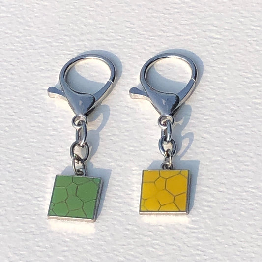 Two square-shaped keychains with green and yellow patterns on a white background