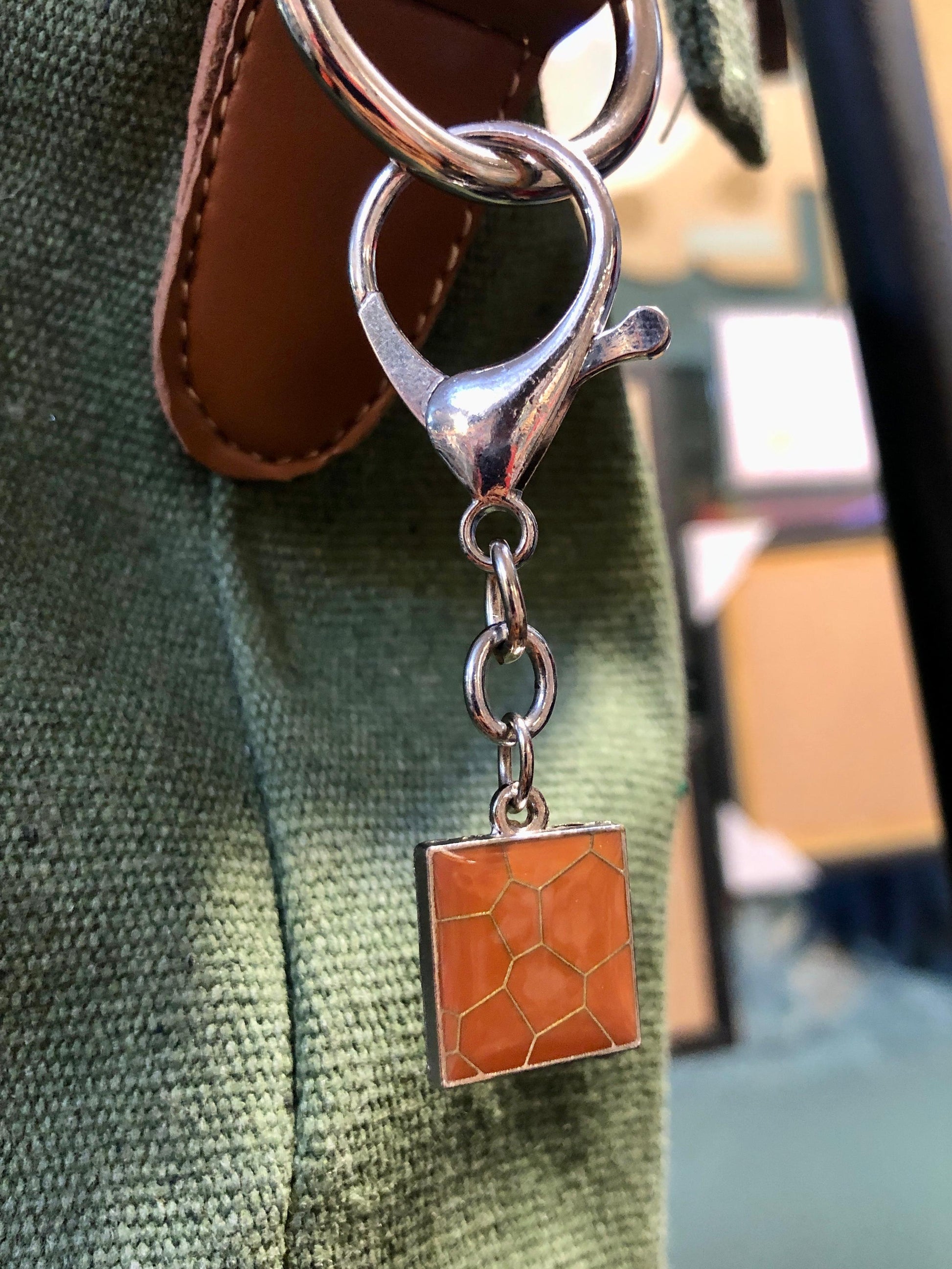Silver keychain with a square orange charm on a green fabric background