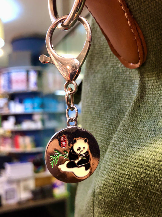 Keychain with panda charm attached to a leather strap, blurred store interior in the background