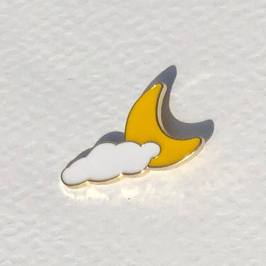 Enamel pin with a design of a crescent moon and cloud on a textured white background