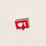 Red enamel pin with heart and number design on a beige background