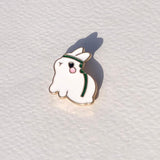 Ghost-shaped enamel pin with a green headband on a white textured background