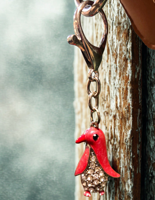 Red bird-shaped keychain attached to a leather strap on a wooden surface